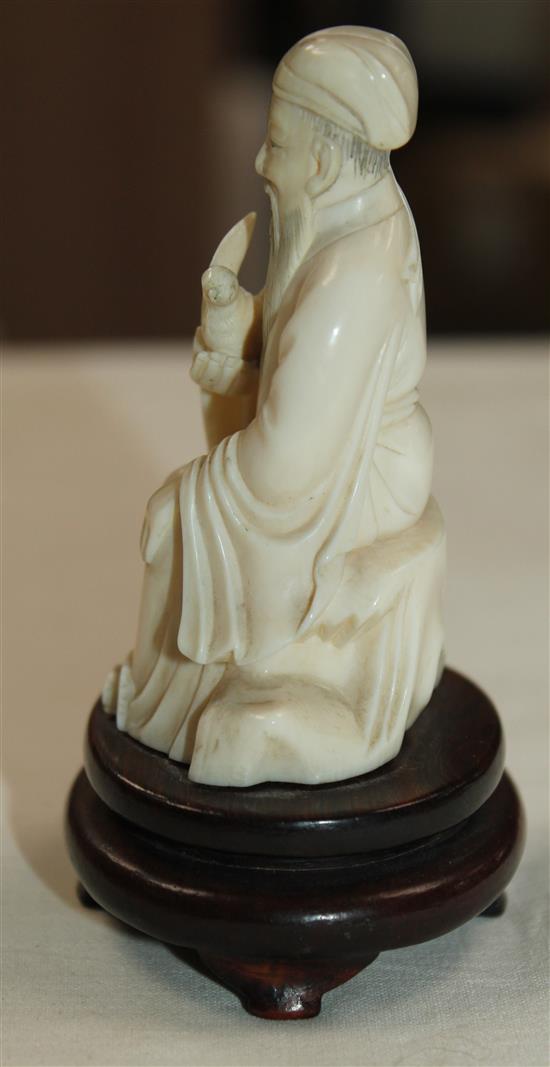 A Chinese ivory seated figure of a scholar holding a bird, early 20th century, wood stand, total height, 10cm